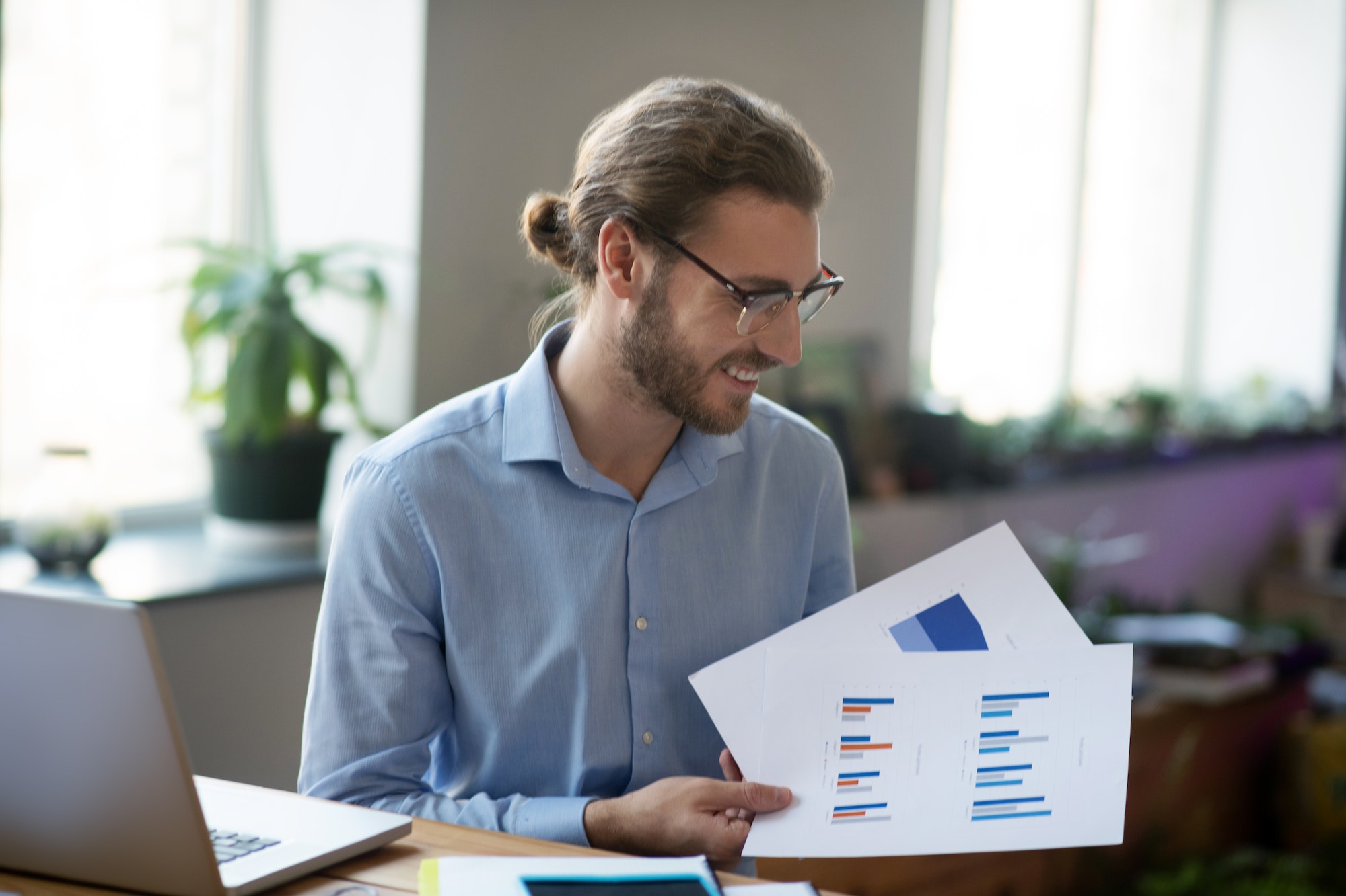 Joyful man near a table with laptop with charts in hand.